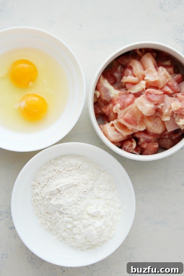 Raw chicken thighs, eggs, flour, cornstarch, and salt arranged on a wooden board, ready for preparing Korean fried chicken.