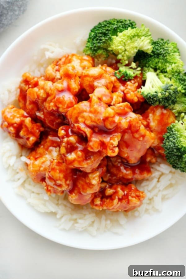 Overhead shot of Korean fried chicken generously coated in Gochujang sauce, garnished with sesame seeds and green onions, served in a rustic bowl.
