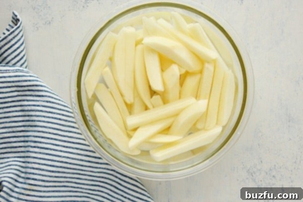Freshly cut potato fries soaking in a bowl of water, an essential step before air frying.