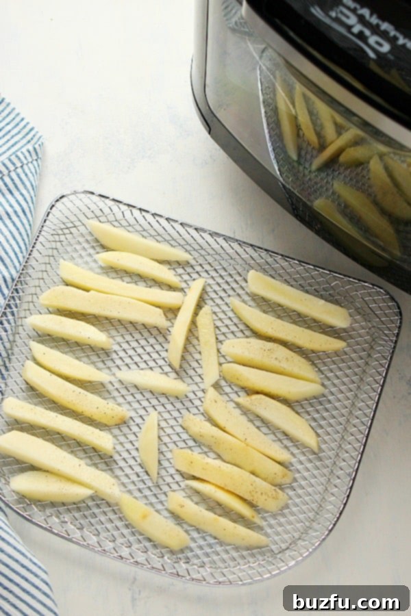 Crispy homemade French fries spread evenly on an air fryer rack, cooking to perfection.