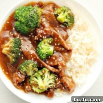 Overhead photo of finished dish of beef and broccoli with rice in a white bowl on white board.