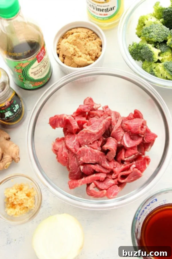 A cutting board with various ingredients for beef and broccoli, including sliced beef, fresh broccoli, onions, garlic, and sauce components.