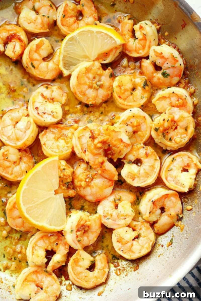 Cooked shrimp in garlic butter sauce with lemon in a skillet.