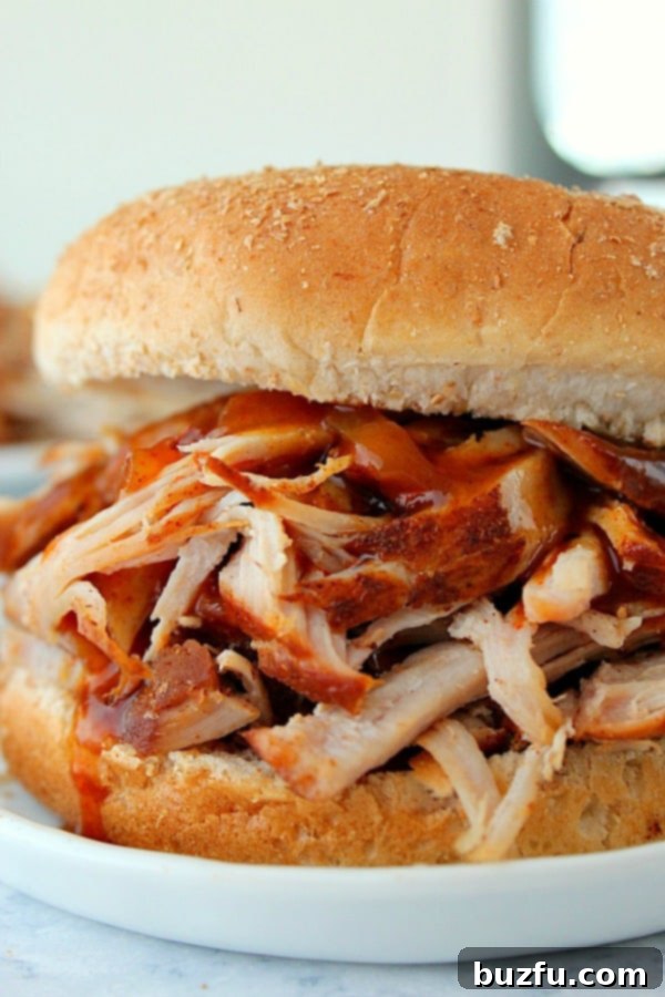 Generous serving of Instant Pot Pulled Pork in a soft bun, presented on a clean white plate.