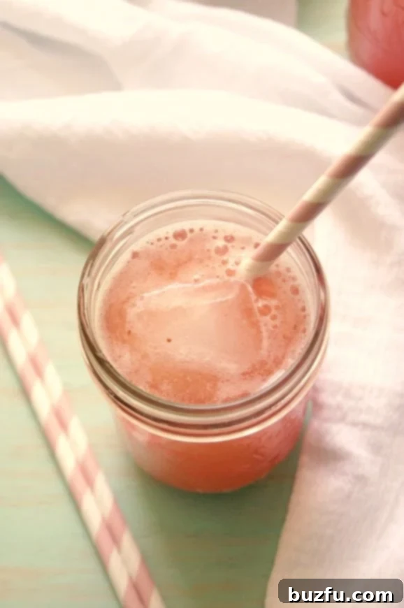 Homemade Strawberry Agua Fresca: A vibrant and delicious way to stay cool. An aerial view of a glass jar filled with luscious strawberry agua fresca, adorned with a straw and surrounded by scattered fresh strawberries on a rustic wooden table.