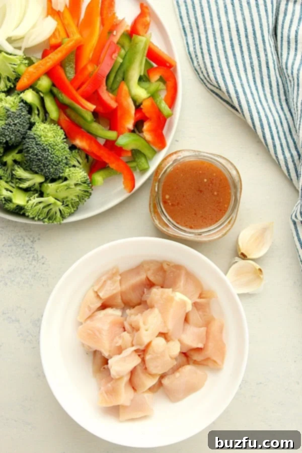 Assortment of fresh ingredients for stir fry, including chicken, broccoli, bell peppers, and onion on a white board.