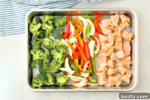 Raw broccoli, bell peppers, and chicken pieces neatly arranged on a baking pan, ready for the oven.
