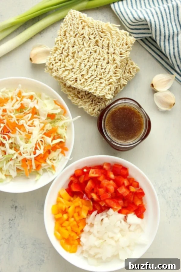 Fresh ingredients for a ramen stir fry laid out on a white cutting board, including ramen noodles, various bell peppers, garlic, ginger, and cabbage.
