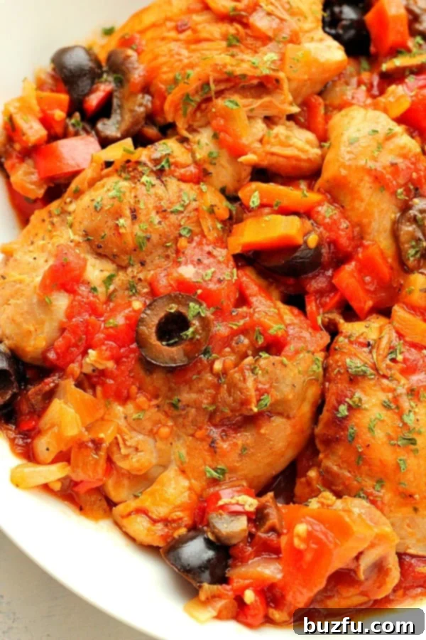 Chicken with tomato sauce, veggies on a white plate.