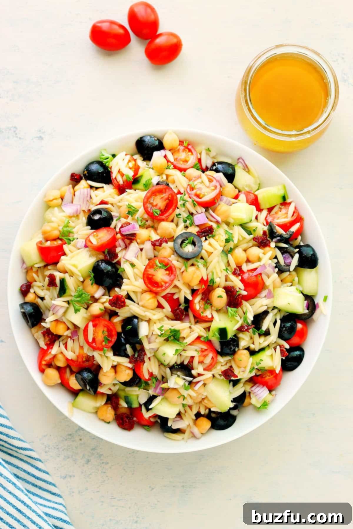 A close-up of Orzo Pasta Salad ingredients like orzo, tomatoes, cucumbers, and olives mingling in a bowl.