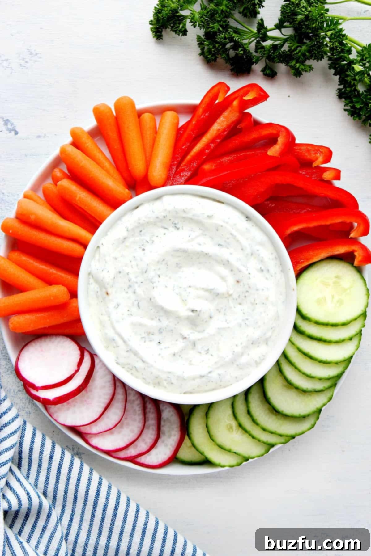 A beautifully arranged platter featuring a white bowl of creamy veggie dip at its center, surrounded by an abundant assortment of fresh, vibrant, and colorful vegetables, all ready for a healthy and delicious snack or party appetizer.