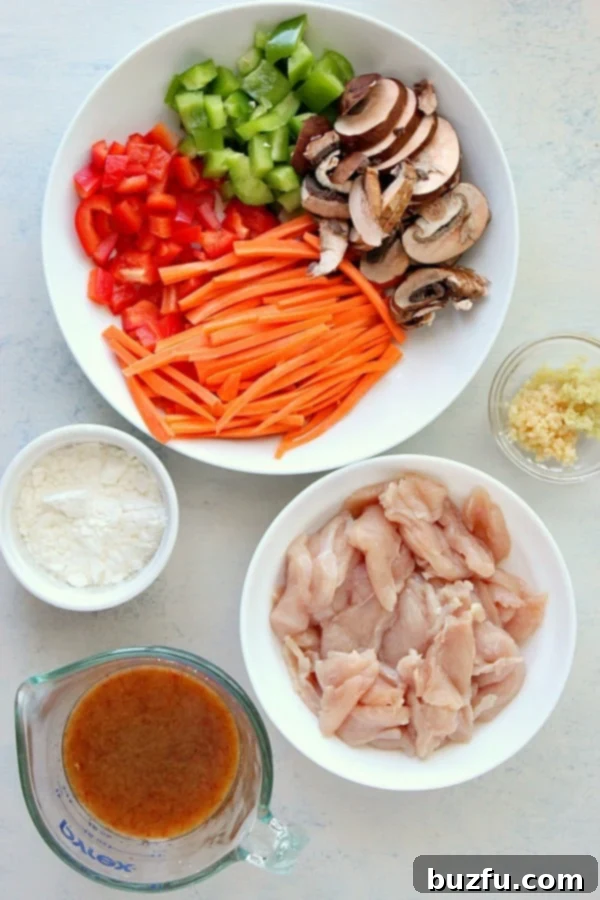 Sliced chicken, chopped bell peppers, broccoli, carrots, and mushrooms arranged on a white cutting board for Hunan Chicken.