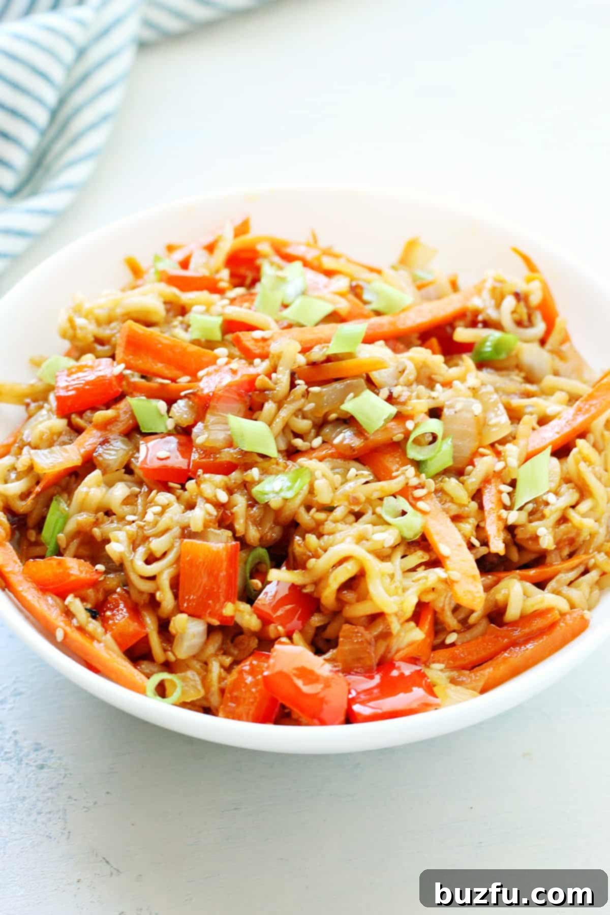 A vibrant bowl of easy pan-fried noodles with mixed vegetables, garnished with sesame seeds and green onions.