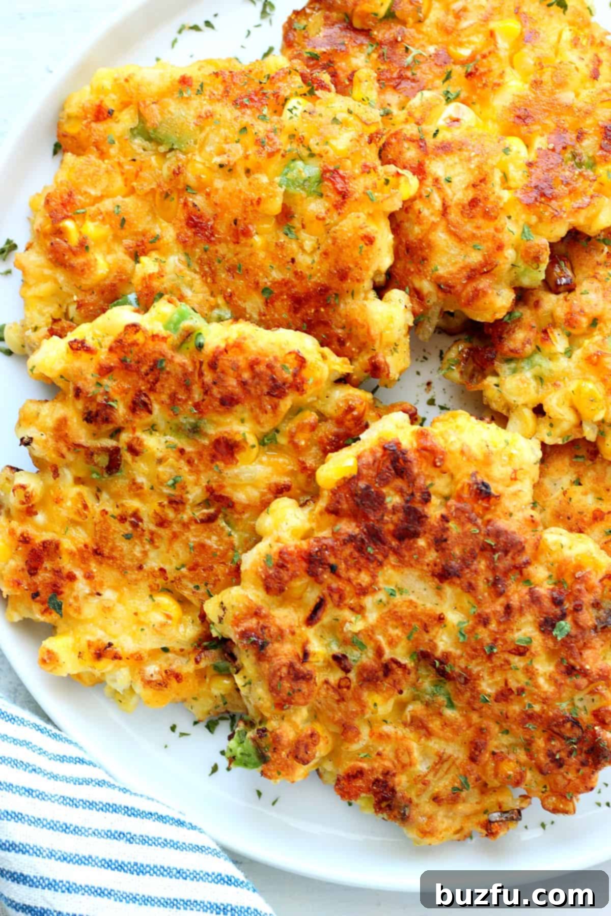 Best Corn Fritters Recipe Crispy golden corn fritters piled on a plate, garnished with fresh herbs.