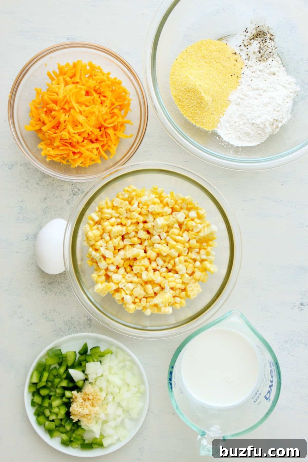 What you need to make corn fritters. Separate bowls containing fresh corn, flour, cornmeal, cheese, and vegetables ready for mixing.