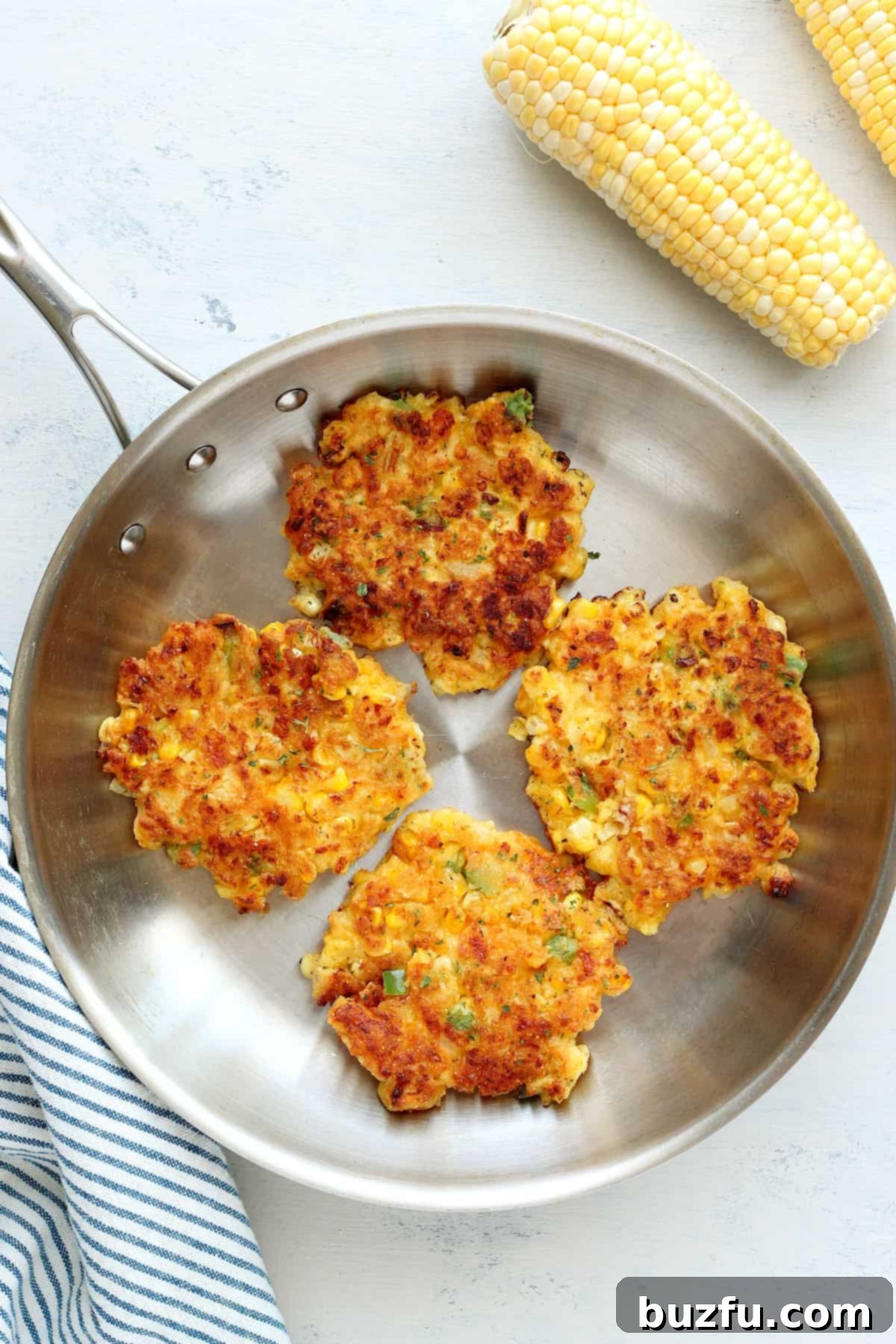 How to fry corn fritters. Several corn cakes frying in a hot pan until golden brown.