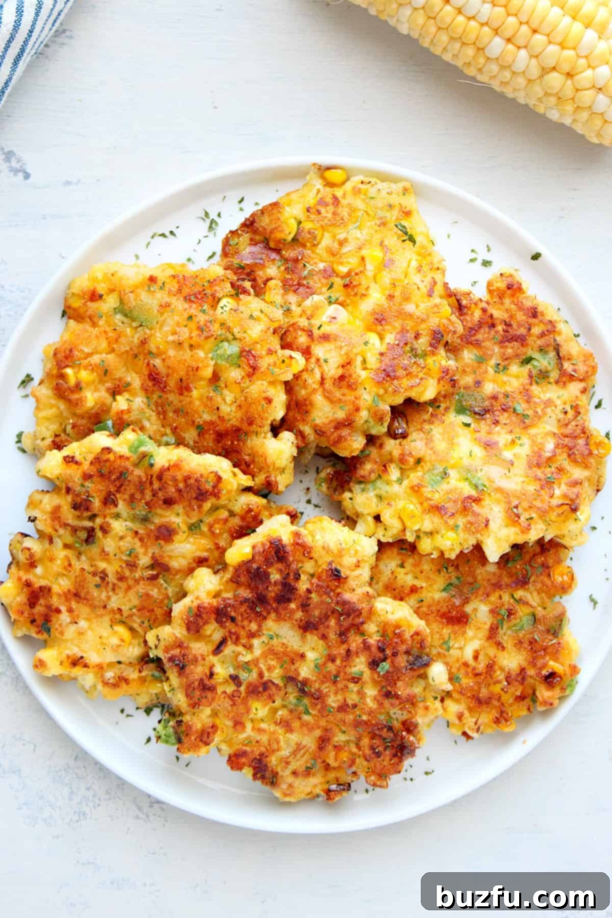 Delicious Corn Fritters Recipe Several crispy corn fritters artfully arranged on a white plate with a side of dipping sauce.