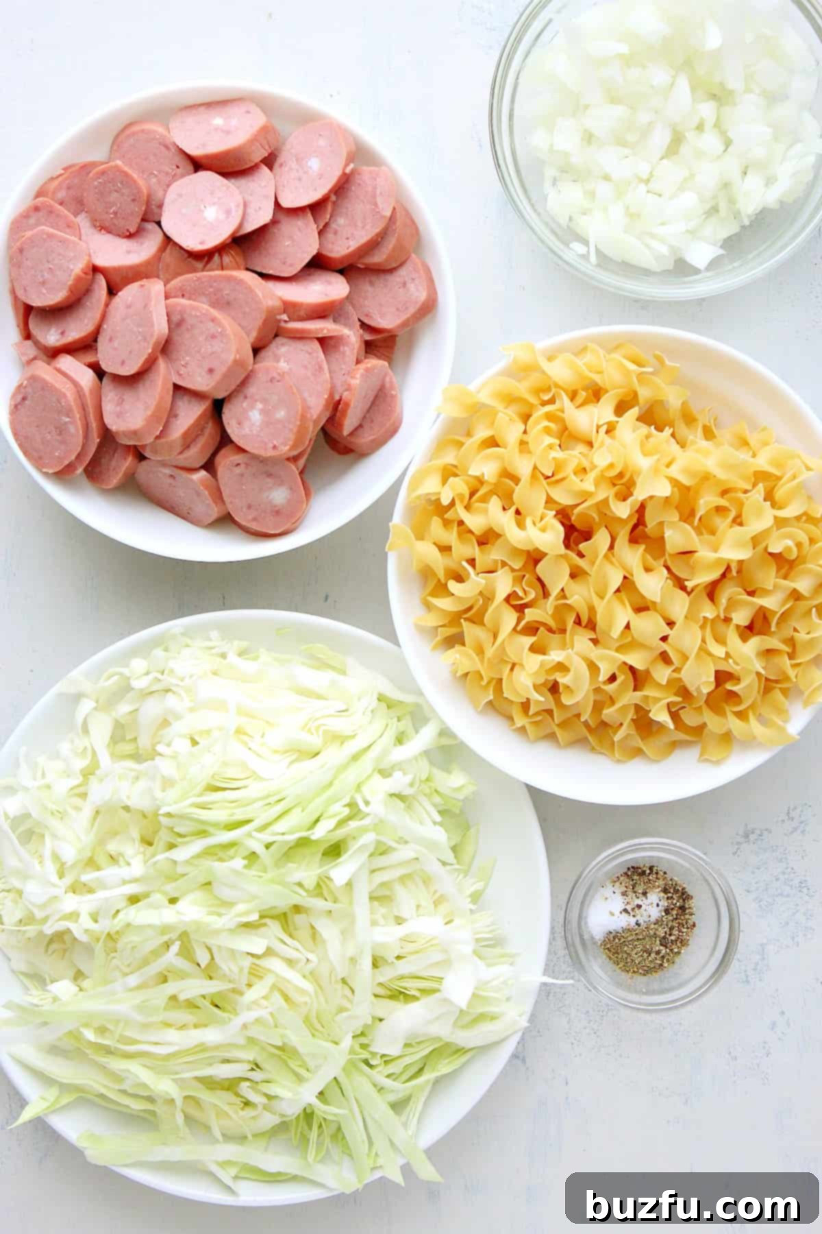 Ingredients for cabbage and noodles recipe laid out on a white cutting board.