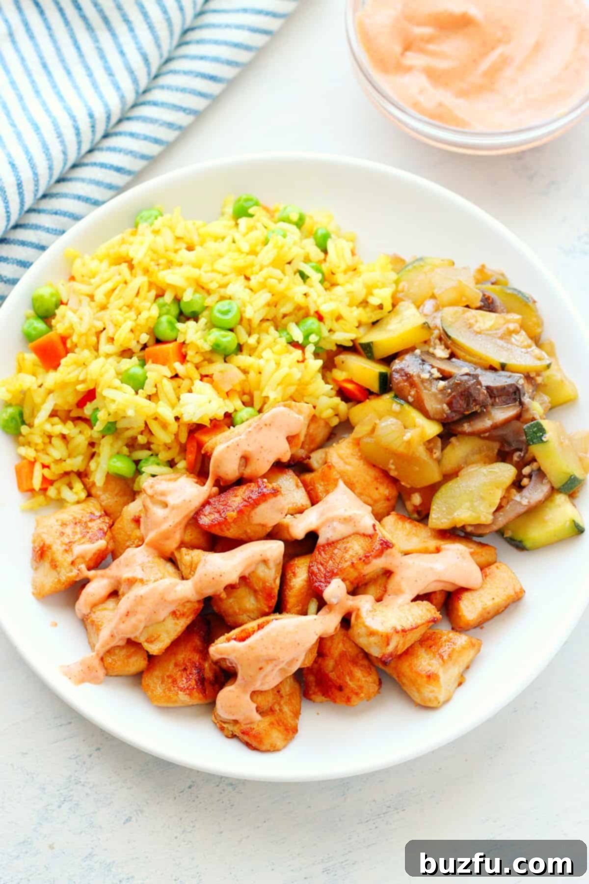 A beautifully plated dish of hibachi chicken, golden fried rice, and brightly colored sauteed vegetables, ready to be enjoyed.