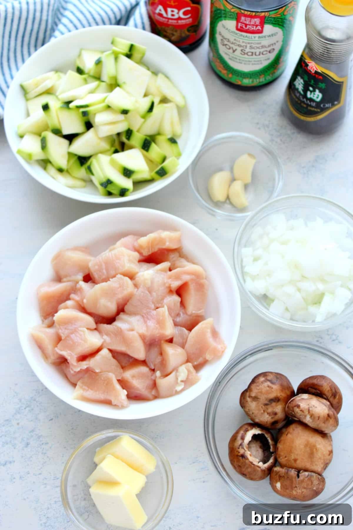 A vibrant selection of fresh ingredients including chopped chicken, zucchini, mushrooms, onions, and seasonings, neatly arranged on a wooden board.