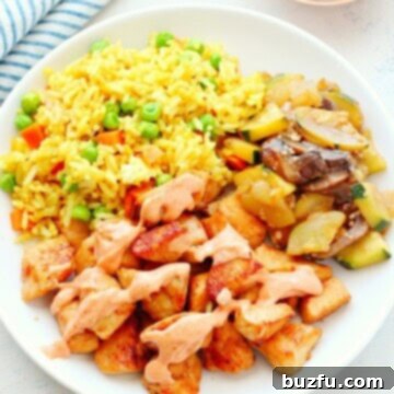 Hibachi chicken, fried rice, and sauteed veggies on a plate.