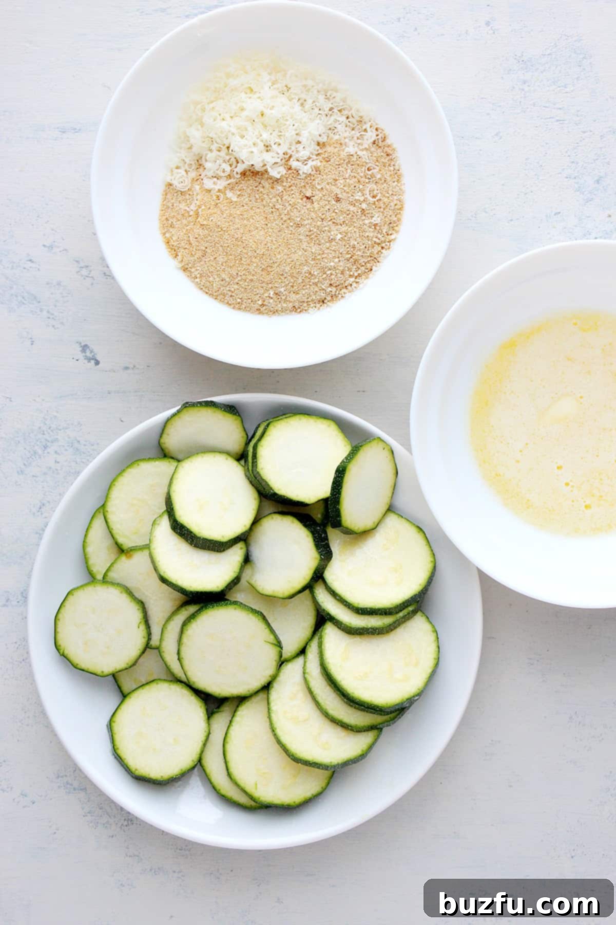 Fresh ingredients laid out on a wooden board, including zucchini, butter, breadcrumbs, and Parmesan cheese.