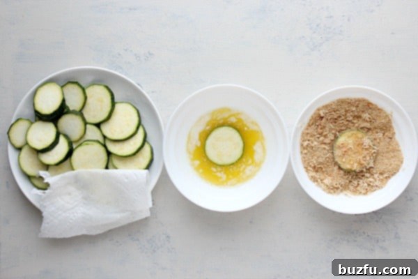 A breading station showing zucchini slices being coated in melted butter and a Parmesan breadcrumb mixture.