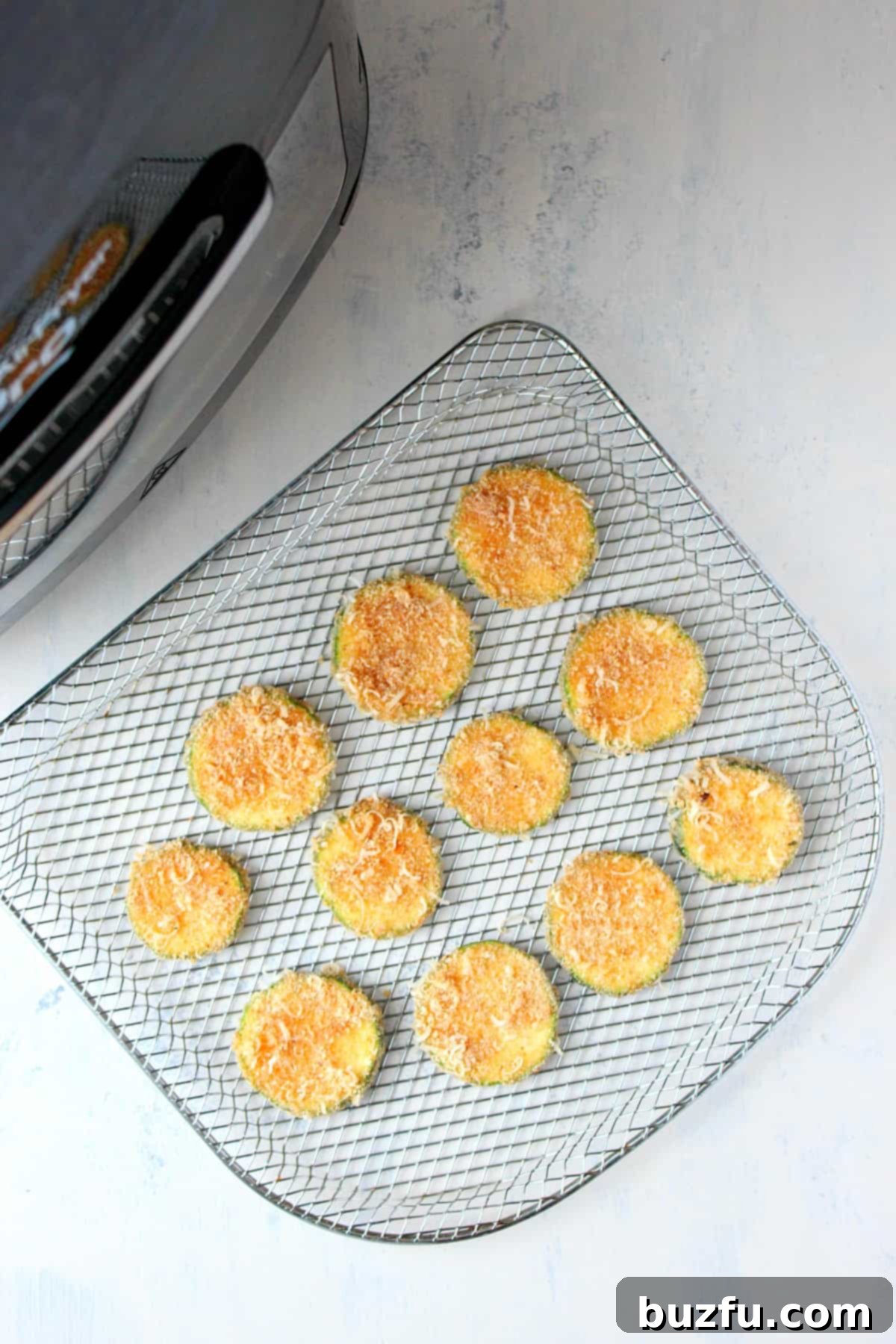 Breaded zucchini slices arranged in a single layer on an air fryer rack, ready for cooking.