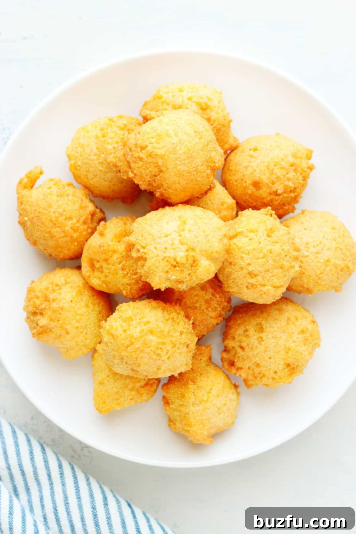 Homemade hush puppies served on a white plate on a wooden board.