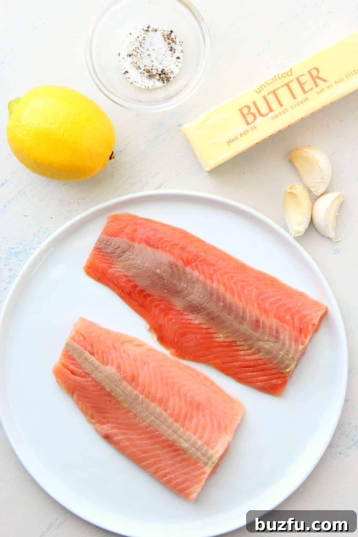 A selection of fresh ingredients including salmon fillets, sliced lemon, minced garlic, and butter, ready for making salmon foil packets.