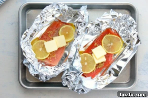Several neatly sealed salmon foil packets resting on a baking sheet, ready to be placed in the oven.