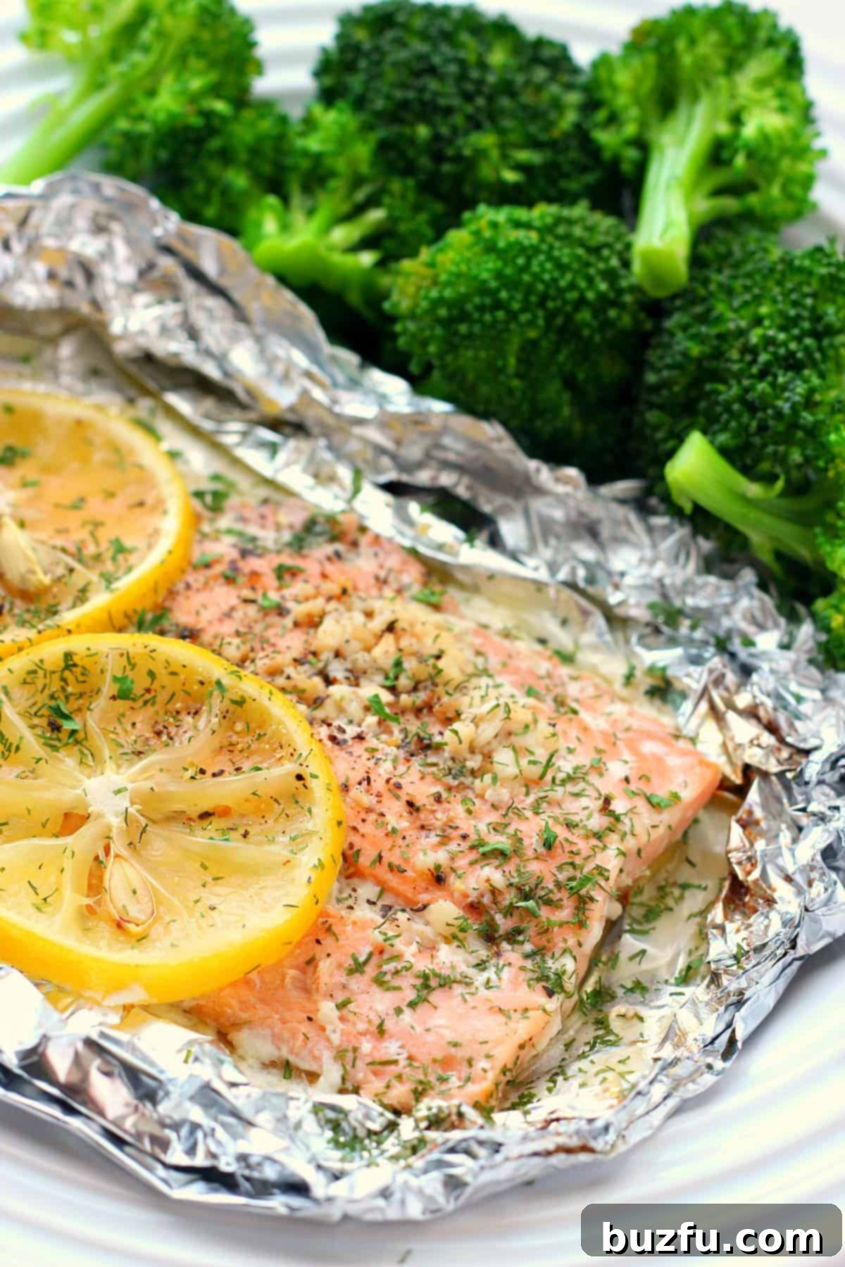 Close-up of a perfectly cooked salmon fillet with bright lemon slices and fresh herbs resting on an opened foil packet.