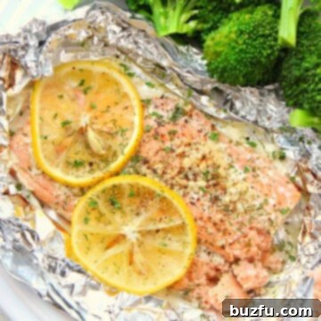 Freshly baked salmon in foil, garnished with lemon slices and herbs, on a white plate.