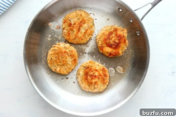 Pan-frying salmon patties for a golden finish Salmon cakes sizzling in a pan on the stovetop.