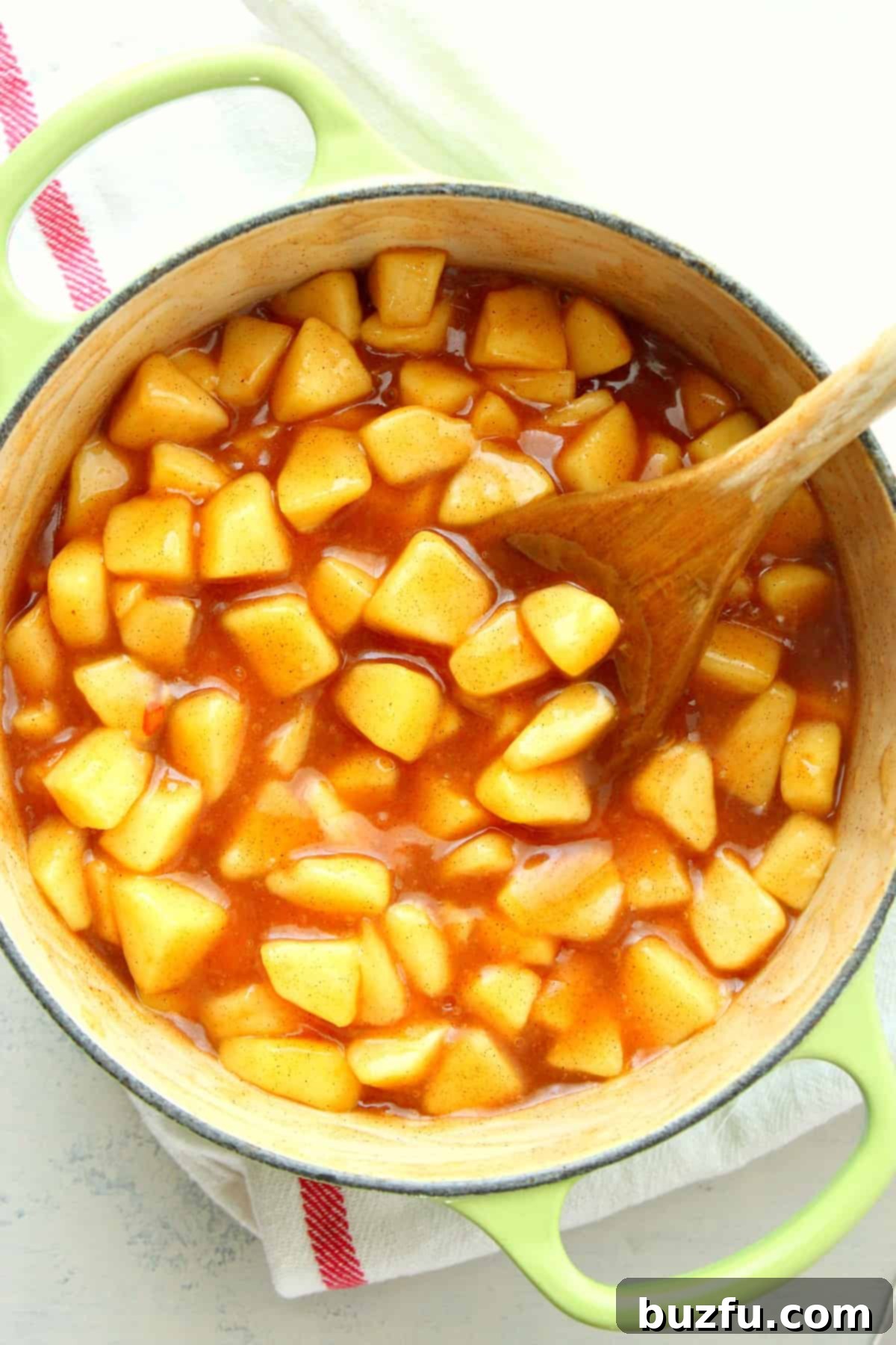 Rich, golden apple pie filling simmering in a rustic Dutch oven, ready for baking, with a wooden spoon resting inside.