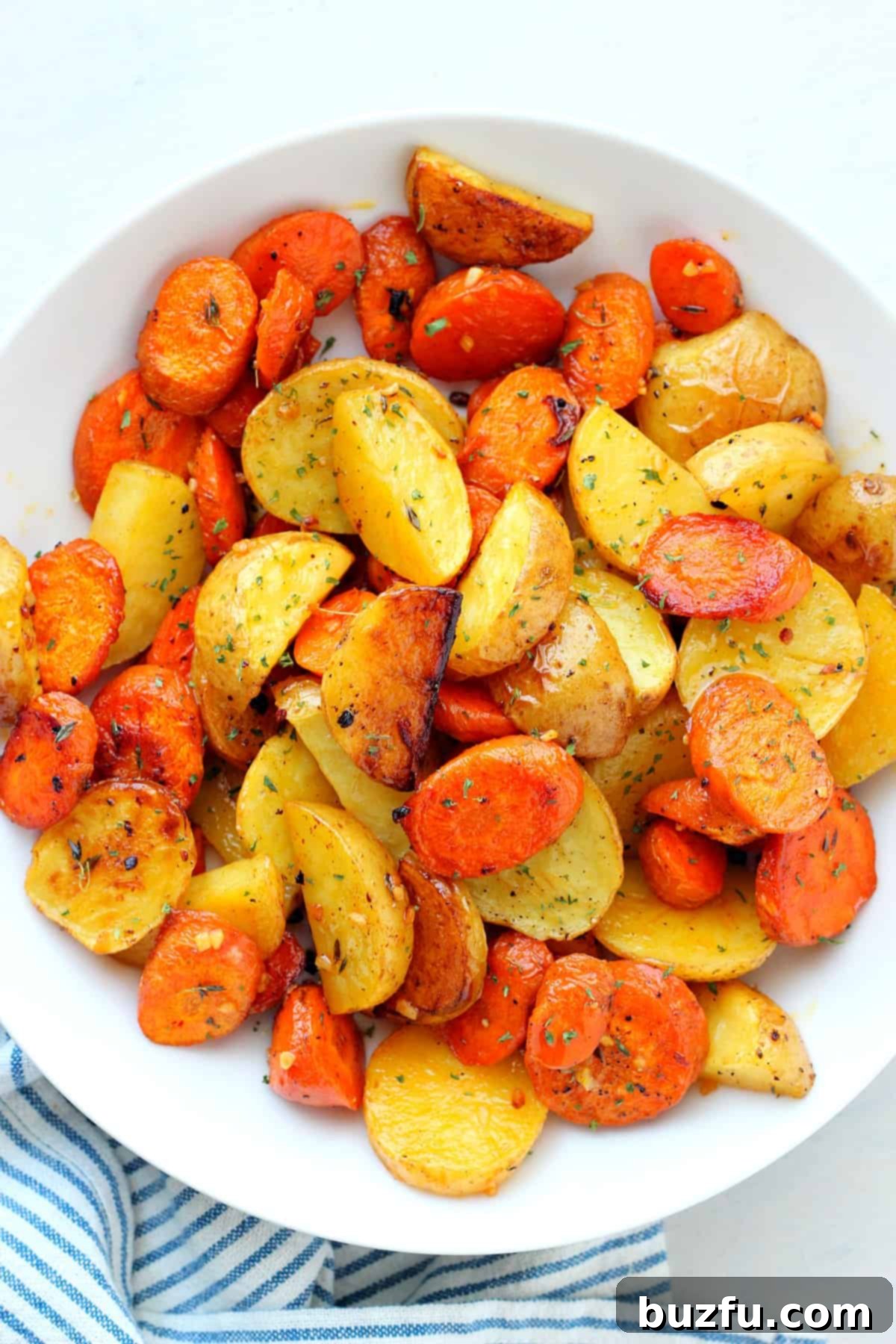 Easy Garlic Butter Roasted Potatoes and Carrots Recipe Close-up of golden brown roasted potatoes and carrots in a white serving bowl, garnished with fresh herbs.