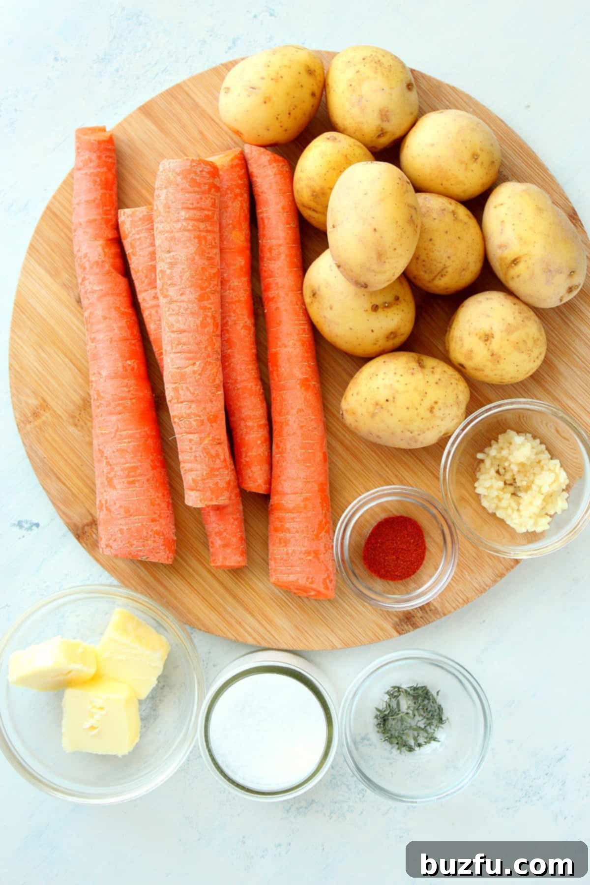 Ingredients for Roasted Potatoes and Carrots Recipe Assortment of baby potatoes and whole carrots laid out on a round wooden cutting board, ready for preparation.