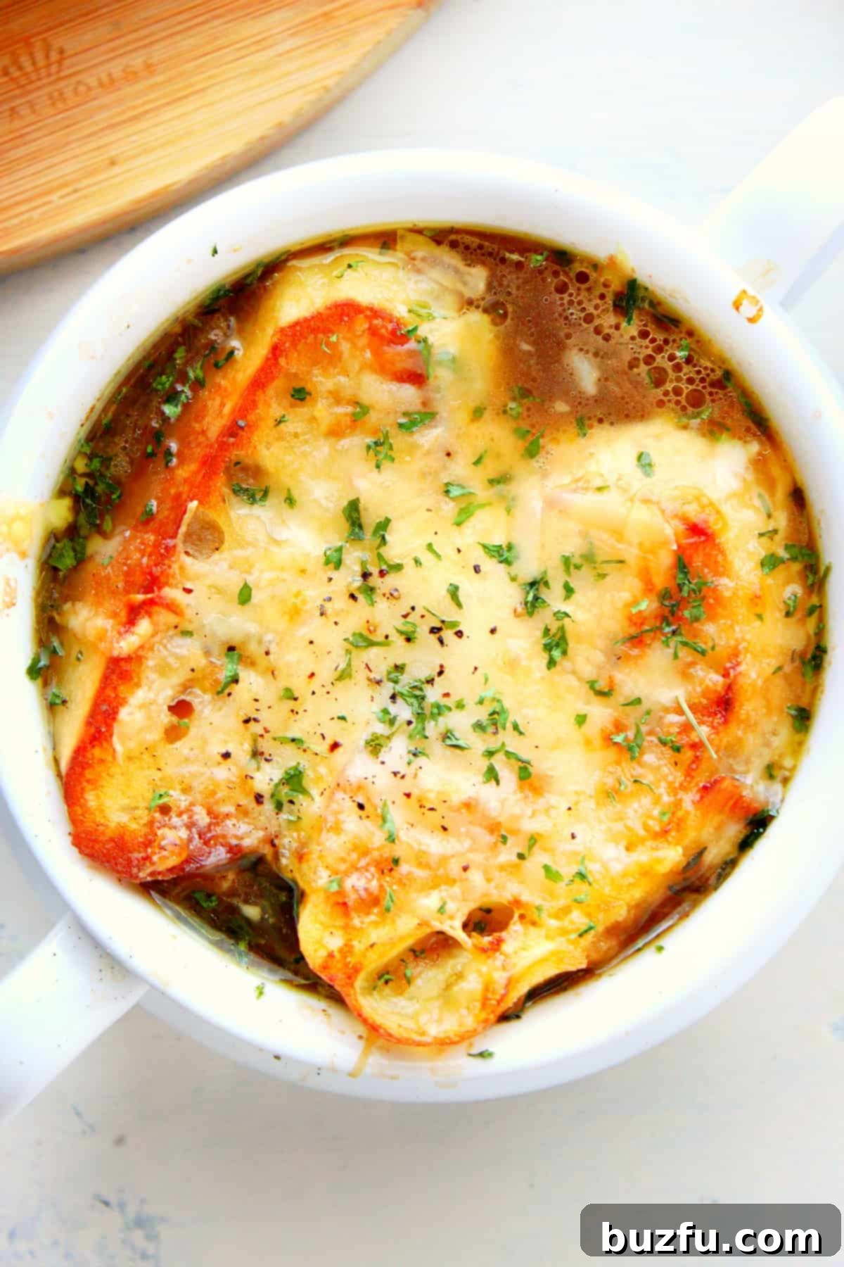 French onion soup with a golden-brown cheesy toast topping in a rustic bowl.