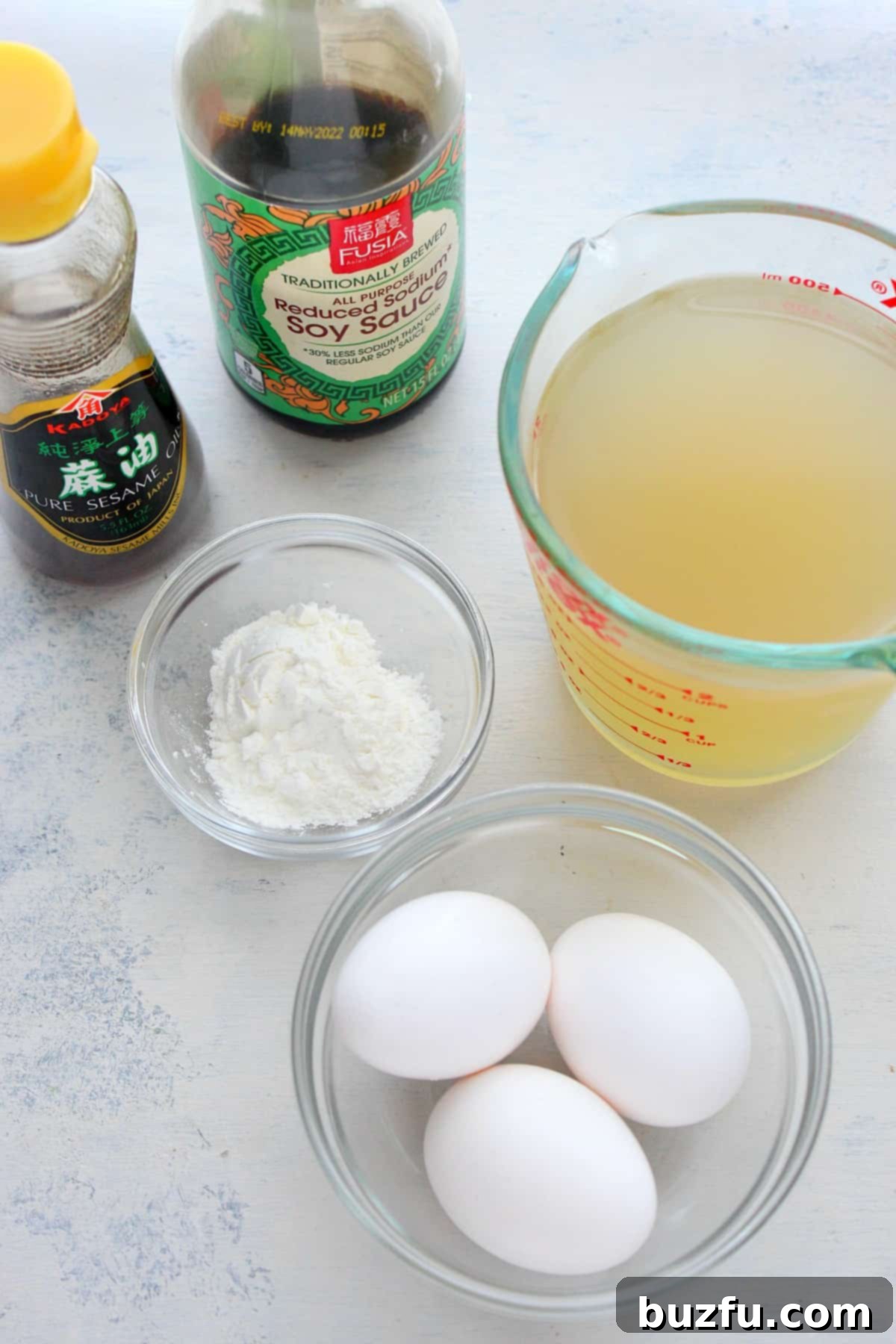 Egg Drop Soup Ingredients Preparation Fresh ingredients for Egg Drop Soup laid out on a wooden cutting board, including chicken stock, eggs, soy sauce, cornstarch, sesame oil, and green onions.