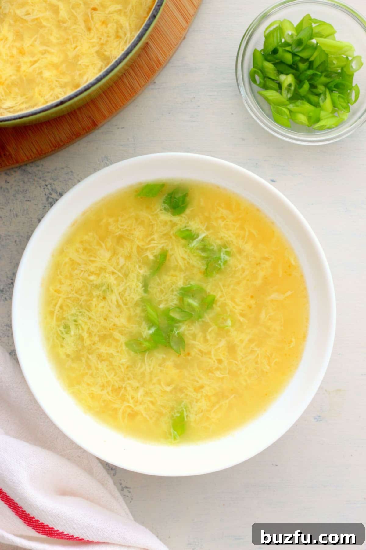 Simple and Delicious Egg Drop Soup A simple white bowl filled with freshly made Egg Drop Soup, garnished with a few sprigs of green onion, ready to be enjoyed.