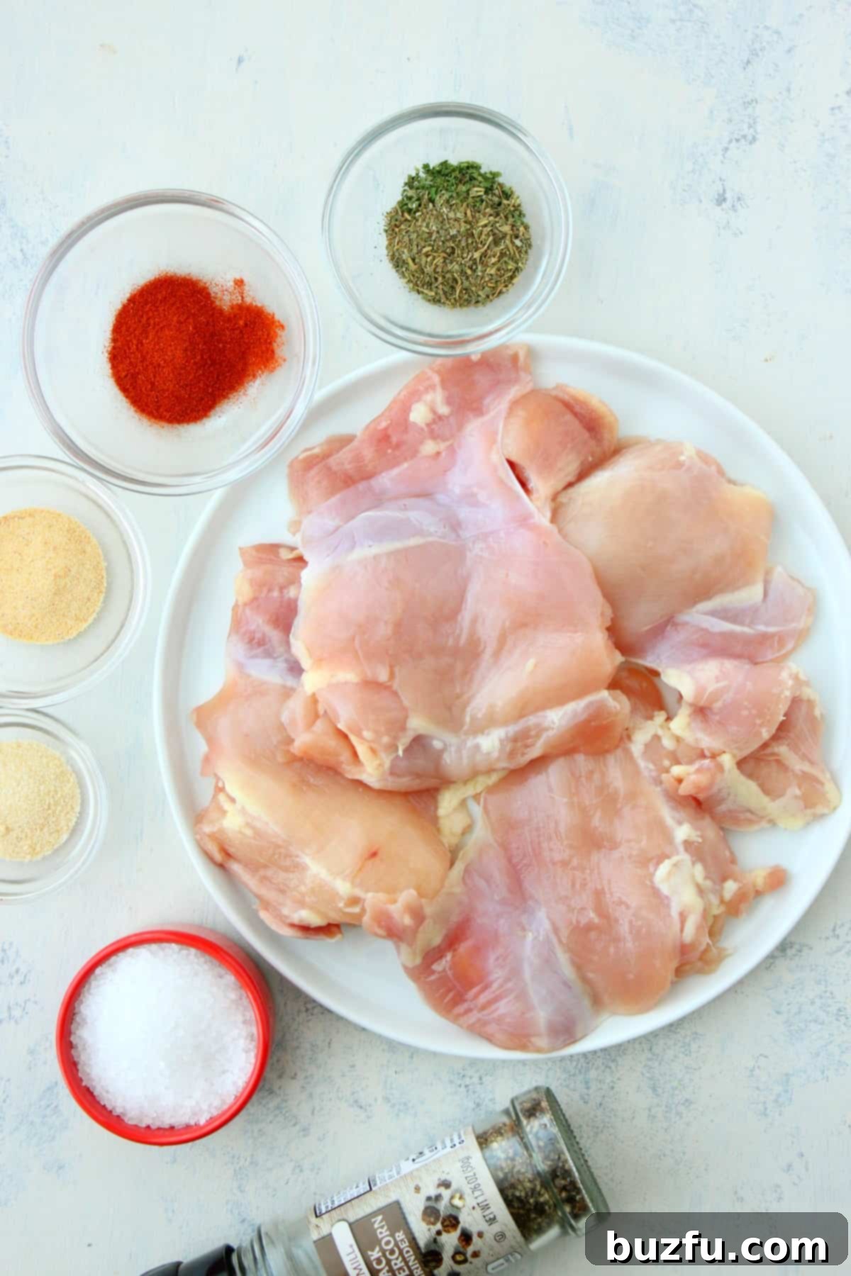 Skillet chicken thighs ingredients Chicken thighs and various spices laid out on a white cutting board.