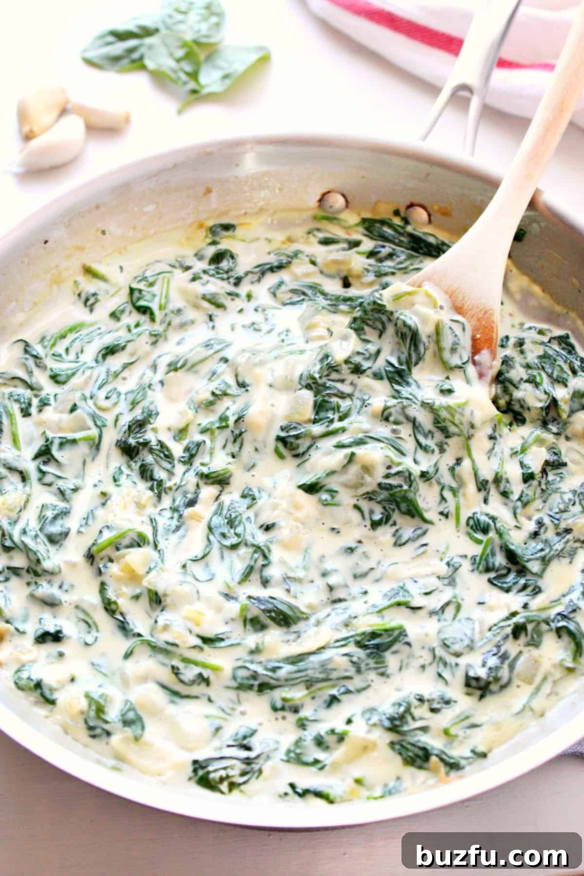 Creamy spinach in a skillet with a wooden spoon, ready to be served.