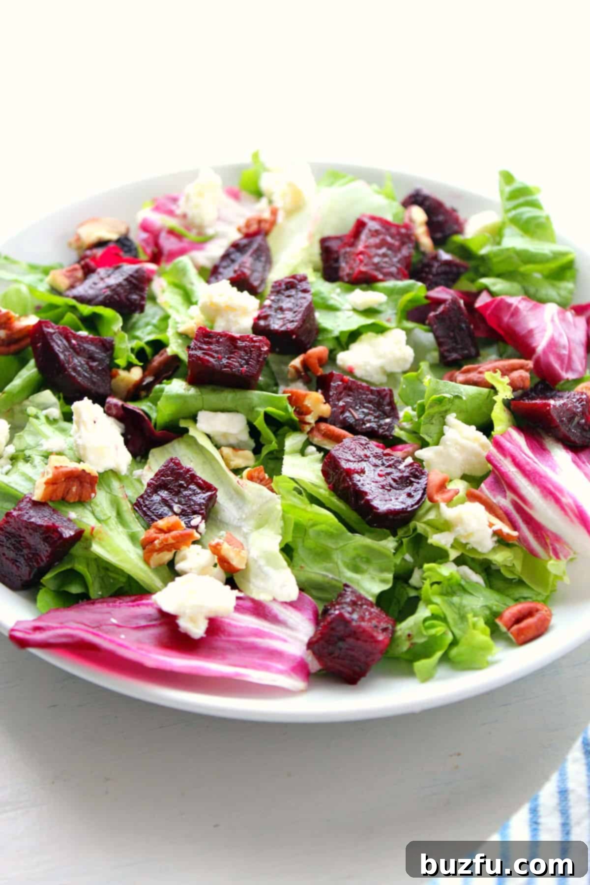 Healthy Beet Salad recipe A vibrant green salad artfully topped with cubes of roasted beets, creamy feta, and crunchy nuts, photographed on a rustic plate.
