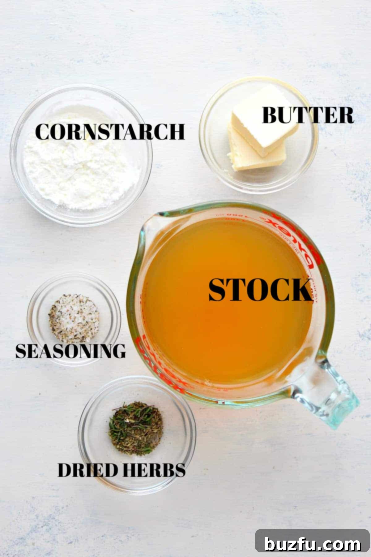 Carefully arranged ingredients for turkey gravy, including cornstarch, butter, turkey stock, various seasonings, and aromatic dried herbs, all presented in elegant glass bowls on a sophisticated gray board.