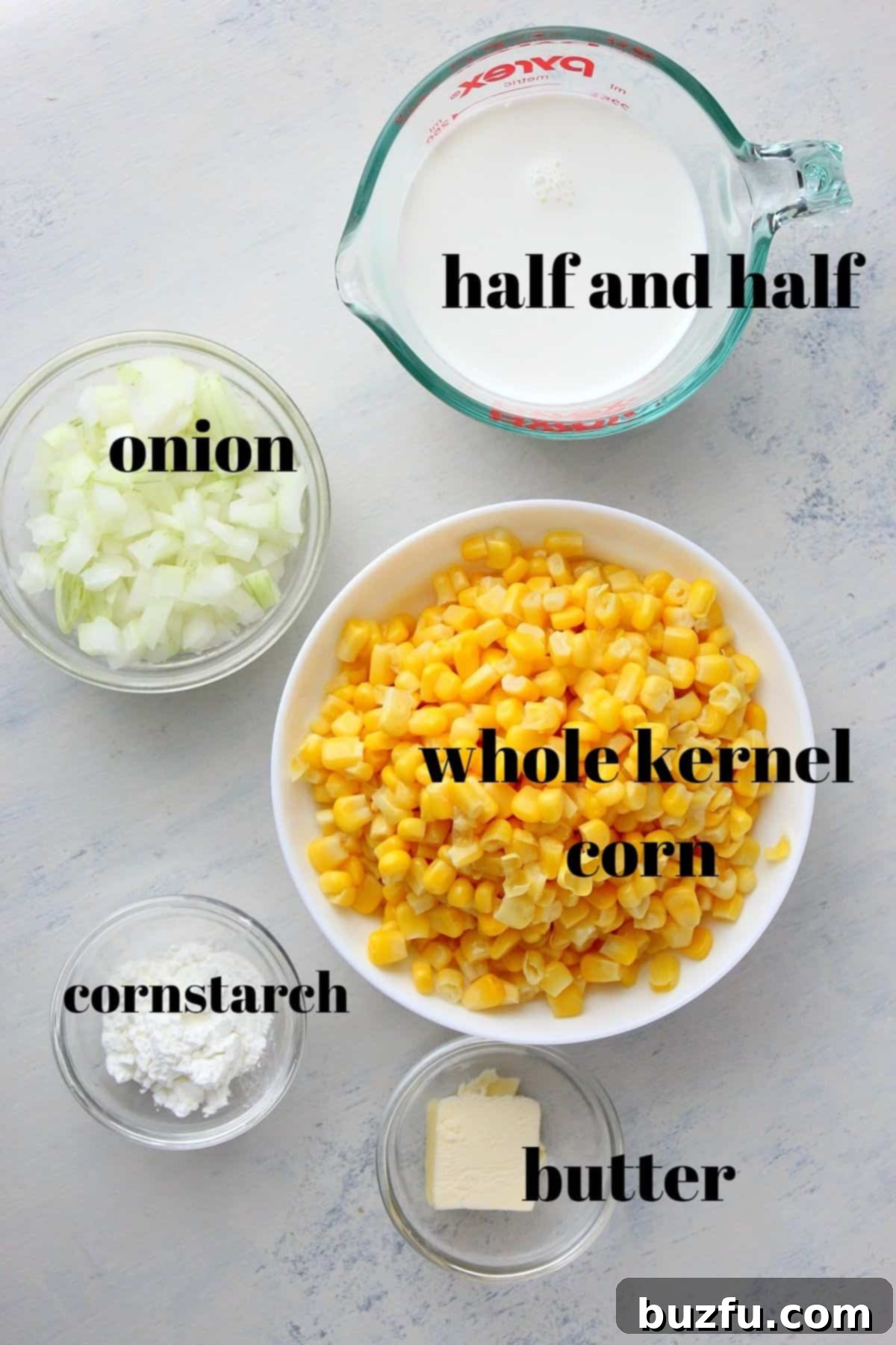 Ingredients for homemade creamed corn laid out on a wooden board, including corn, butter, onion, half and half, and cornstarch.