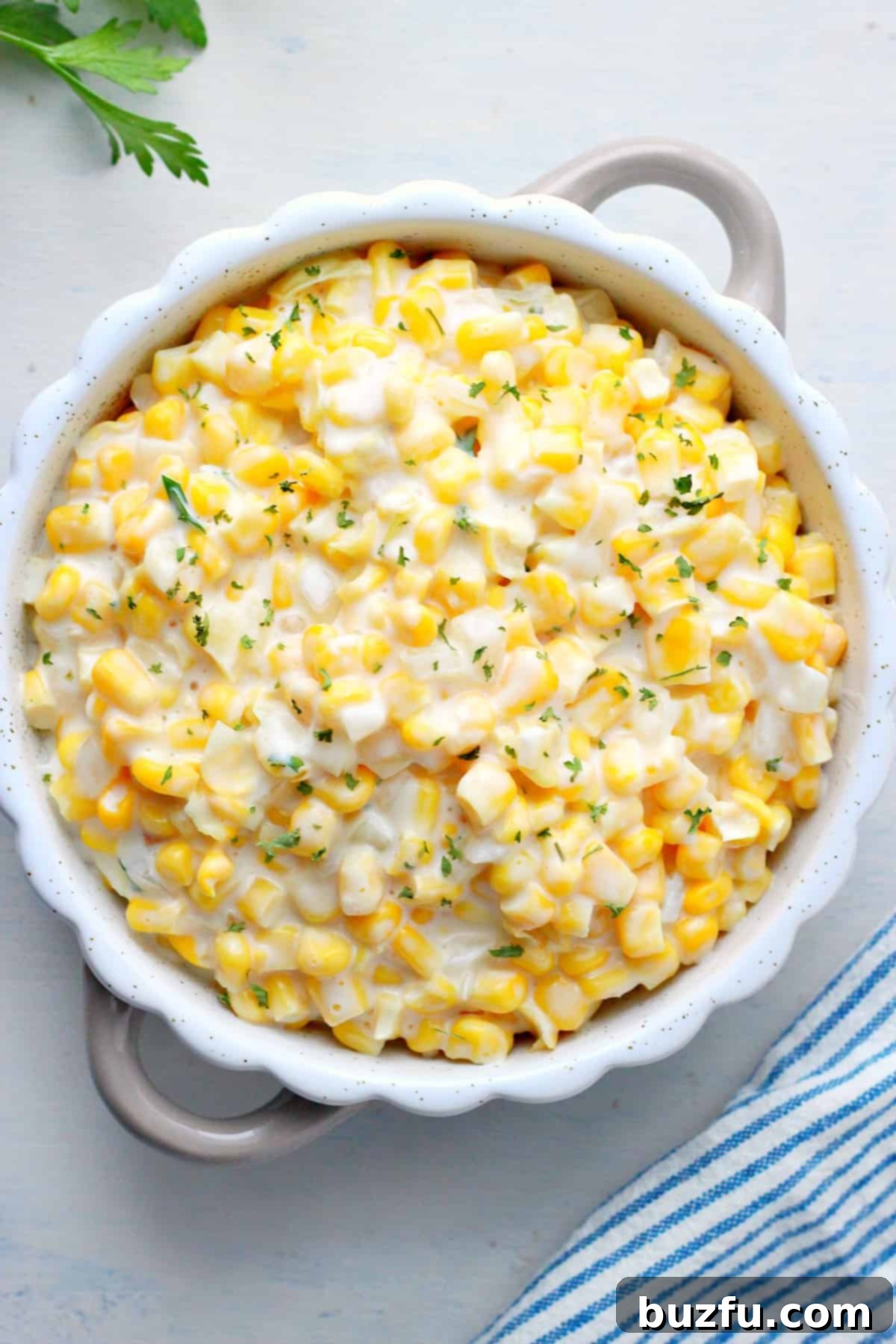 Creamed corn served in a round white dish, garnished with fresh herbs.
