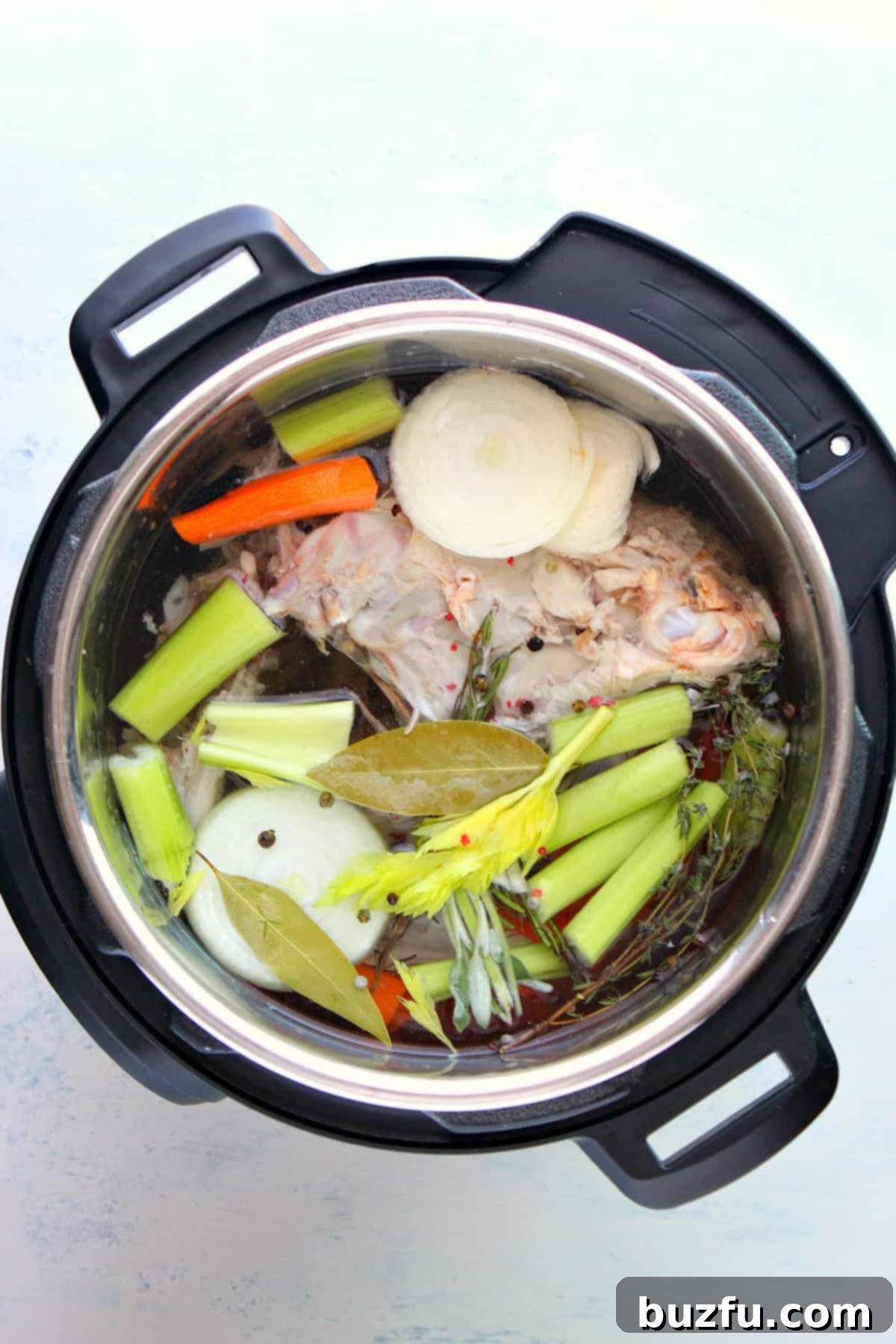 How to make turkey stock in the Instant Pot. Ingredients for making turkey stock laid out on a cutting board, including a turkey carcass, carrots, celery, onion, garlic, and herbs.