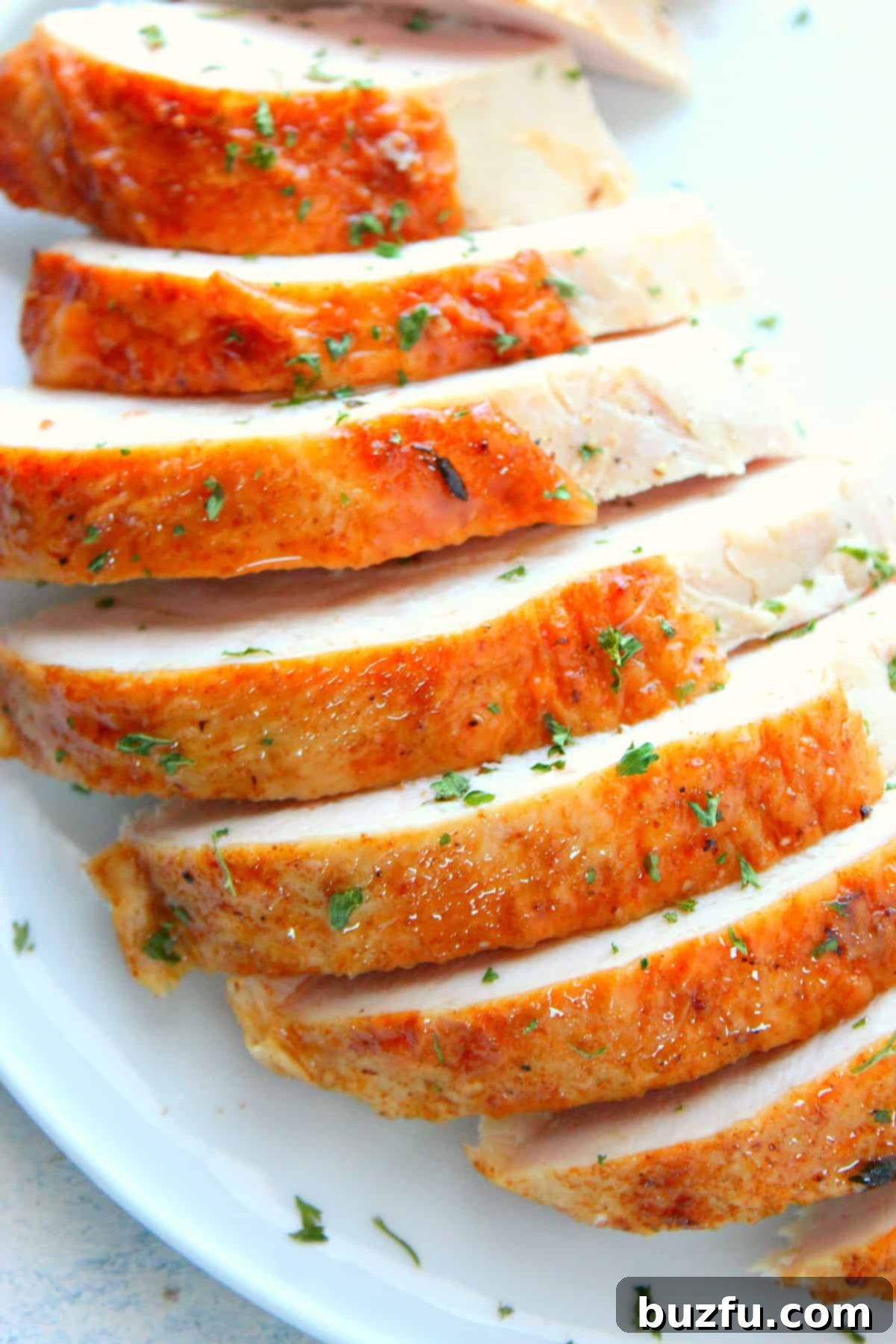 Perfectly sliced turkey breast. Close-up view of beautifully sliced white turkey breast meat, perfectly cooked and arranged on a pristine white serving plate, garnished with fresh herbs.