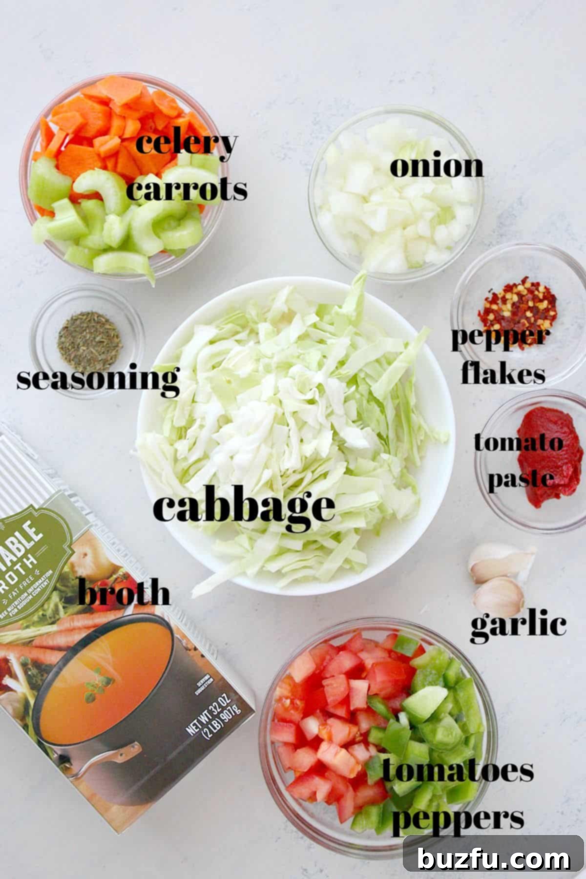 Assortment of fresh vegetables including green cabbage, carrots, celery, onions, tomatoes, and bell pepper laid out on a wooden cutting board, ready for making a vibrant soup.