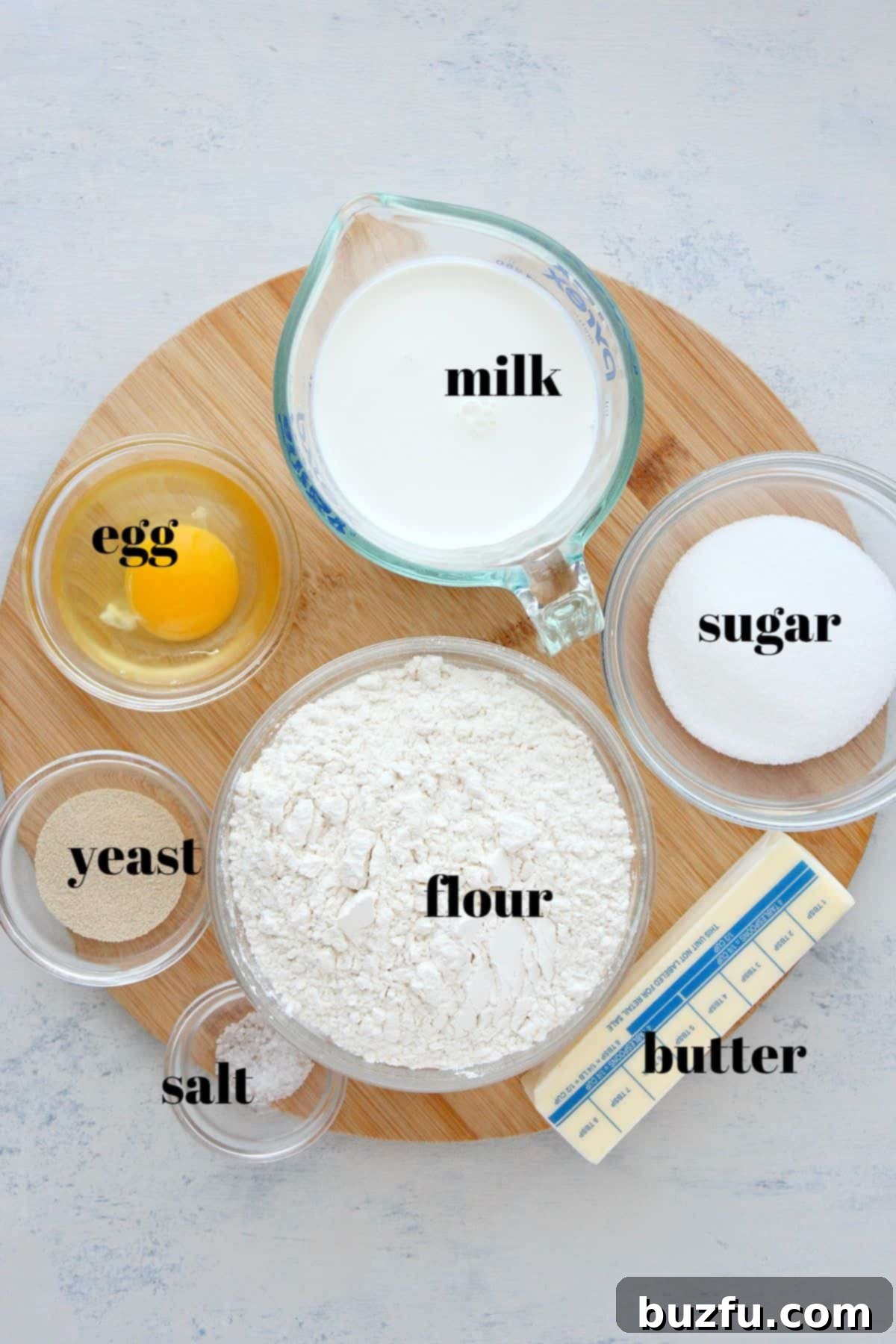 Assortment of fresh ingredients for babka recipe, including flour, sugar, yeast, milk, egg, butter, and salt, neatly arranged on a rustic cutting board.